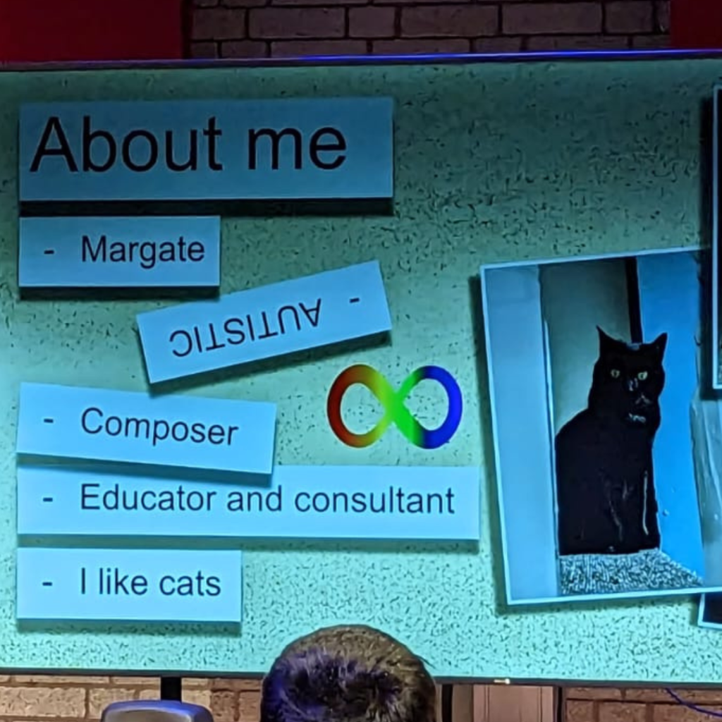 Presentation slide with a picture of a black cat, the Neurodiversity rainbow infinity symbol and the words "About me, Margate, Autistic, Composer, Educator and consultant, I like cats".